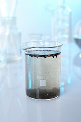 Glass beaker with dirty water and other glassware on mirror surface, closeup