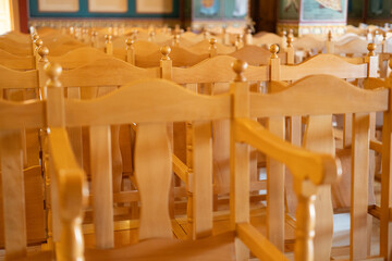 Rows of wooden chairs are organized in an empty hall, illuminated by sunlight. The ambiance is calm and inviting, perfect for gatherings or events.