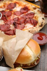 Delicious burger, ketchup and pizza on wooden table, closeup. Tasty fast food