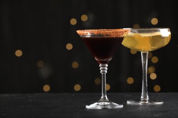 Different martini cocktails in glasses on black table against blurred lights, closeup. Space for text