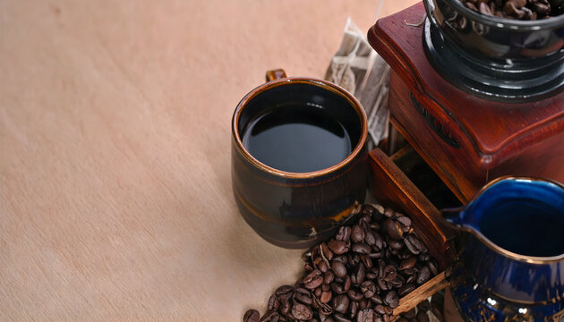 Close-Up of Black Coffee in a Ceramic Mug with Scattered Coffee Beans and Wooden Grinder