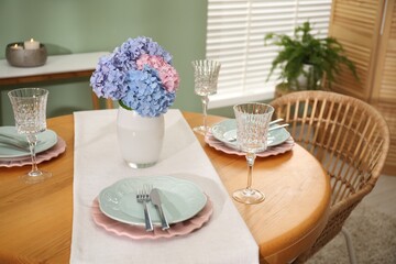 Stylish setting with plates and vase of flowers on wooden table in dining room. Interior design