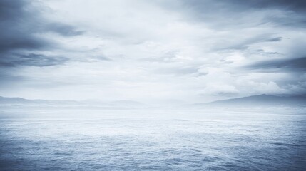 Fototapeta premium A serene coast with calm waters stretches towards the horizon under a sky filled with soft diffused clouds,