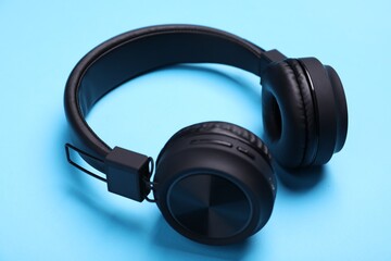 Pair of stylish black headphones on light blue background, closeup