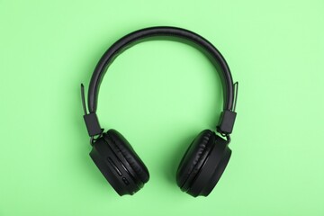Pair of stylish black headphones on light green background, top view