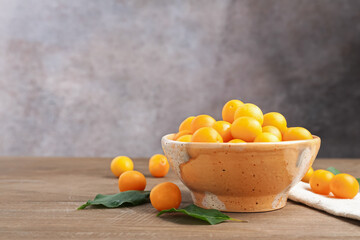 Ripe yellow cherry plums and leaves on wooden table. Space for text