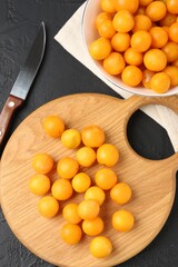 Ripe yellow cherry plums, wooden board and knife on black table, flat lay