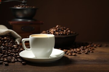 Aromatic coffee in cup, beans and grinder on wooden table against brown background, closeup