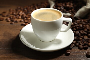 Aromatic coffee in cup and beans on wooden table, closeup