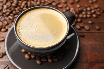 Aromatic coffee in cup and beans on wooden table, closeup