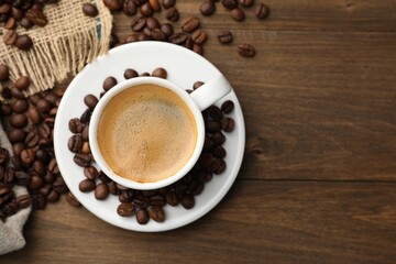 Aromatic coffee in cup and beans on wooden table, flat lay. Space for text