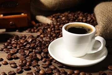 Aromatic coffee in cup and beans on wooden table, closeup
