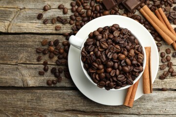 Aromatic coffee beans in cup, cinnamon and pieces of chocolate on wooden table, flat lay. Space for text