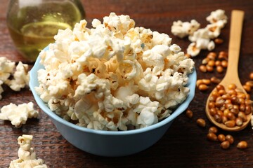 Tasty popcorn, oil and corn kernels on wooden table, closeup