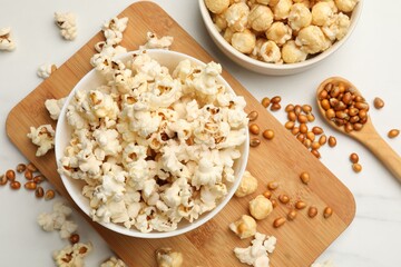 Tasty popcorn and corn kernels on white marble table, flat lay
