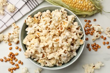 Tasty popcorn, corncob and corn kernels on white marble table, flat lay