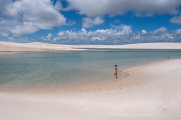 A person walks alone along a tranquil lagoon that separates vast, white sand dunes. A serene moment of solitude and discovery in a surreal landscape