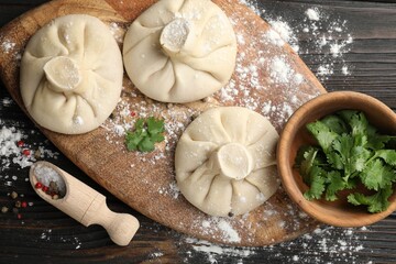 Uncooked khinkalis (dumplings), spices and parsley on dark wooden table, flat lay