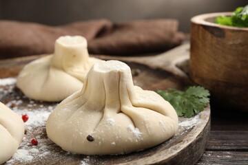 Uncooked khinkalis (dumplings) with peppercorns and parsley on wooden table, closeup