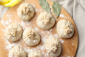 Uncooked khinkalis (dumplings) with flour and bay leaves on table, top view