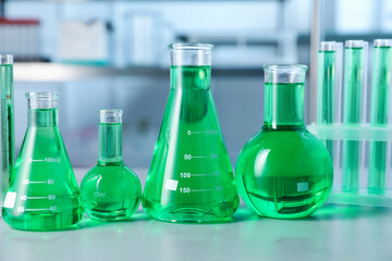 Different laboratory glassware with green liquid on light table indoors