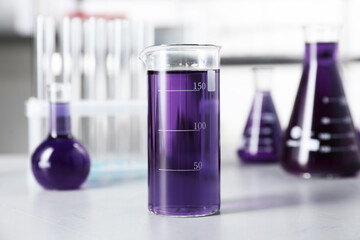 Different laboratory glassware with purple liquid on light table indoors, selective focus