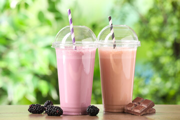 Tasty milkshakes in plastic cups and ingredients on wooden table outdoors