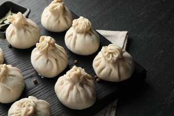 Uncooked khinkalis (dumplings) with peppercorns on black table, closeup