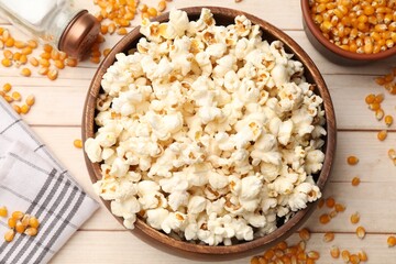 Tasty popcorn and corn kernels on light wooden table, flat lay