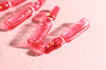 Glass ampoules with liquid and water drops on pink background, closeup