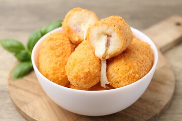 Delicious fried croquettes in bowl and basil on table, closeup