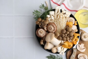 Different raw mushrooms in bowl and dill on white tiled table, flat lay. Space for text