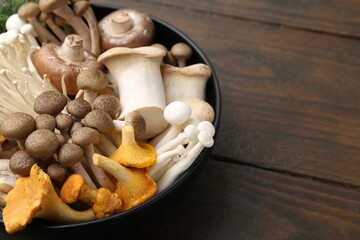 Different raw mushrooms in bowl on wooden table, closeup. Space for text