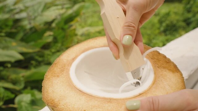 Hand Scraping Soft Coconut Meat Into Thin Strips Using Wooden Tool in Tropical Setting, Close Up, Slow Motion, Vegan Food Concept