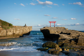 Red torii gate standing on rocks in the sea, connected by rope bridge, shinto shrine, japan