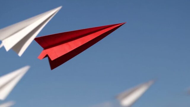 Concepts of transformation and divergence illustrated by solitary crimson origami aircraft veering away from flock of white ones, representing leadership, originality, novel thought, alteration, fash