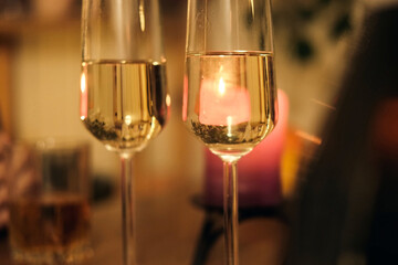 Champagne being poured into champagne flute, bubbles. Sparkling beverage. Romantic Dinner Table with Flickering Candles, Flutes. Warm ambiance. Glasses of champagne. Celebration, Anniversary, Luxury