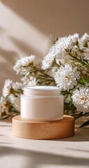 A light beige cream jar sits atop a light wooden coaster, surrounded by a cluster of white flowers, bathed in warm sunlight
