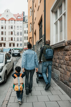 Rear view of family trolling on sidewalk near building at city street