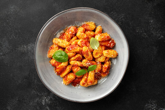 Traditional Italian potato gnocchi with tomato sauce, parmesan cheese and fresh basil leaves on black background, top view	