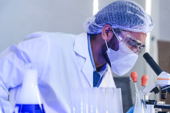 A focused male scientist in full protective gear analyzes a chemical solution in a flask. A dedicated researcher works in a modern laboratory on a medical or pharmaceutical discovery.