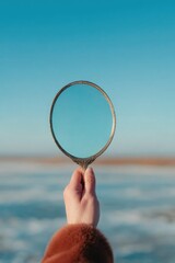 Hand holding circular mirror reflecting clear blue sky over tran