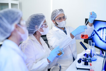 A diverse team of scientists collaborates in a genetics lab. A male researcher explains a procedure...
