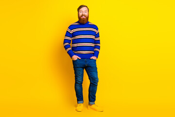Fototapeta premium Stylish man with a red beard in a striped sweater standing on a yellow background exuding cheerful confidence and casual fashion.