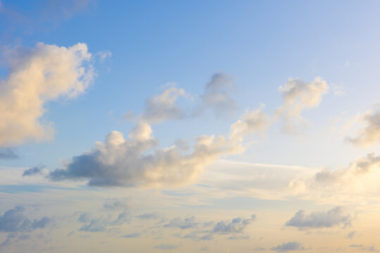 Beautiful cloudscape image of detached fluffy cumulus clouds light blue sky sun setting.