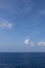 Vertical image of calm peaceful ocean horizon with whimsy white partly cloudy day on the western Caribbean Sea view from cruise ship deck
