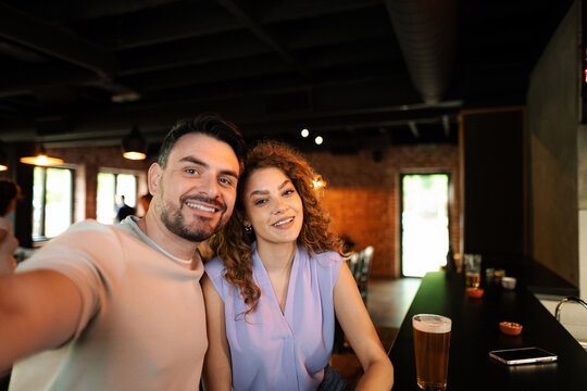 Happy couple taking selfie while drinking beer at the bar counter