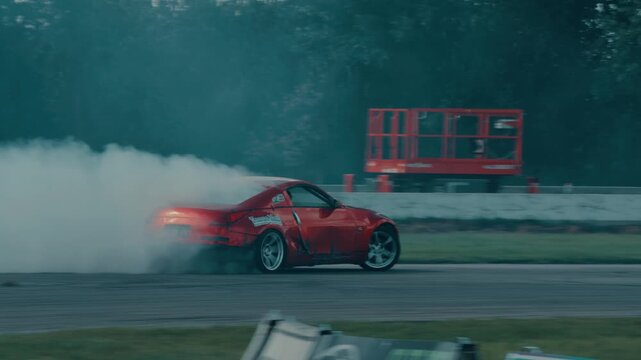 Red sports car drifting on a race track with smoke coming from the tires.
