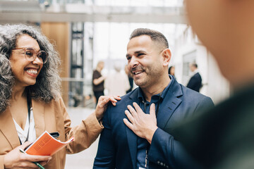 Happy mature businesswoman standing with hand on shoulder of colleague at networking event