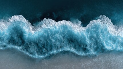 Fototapeta premium Aerial view of ocean waves crashing onto a sandy shore, creating white foam and deep blue water.